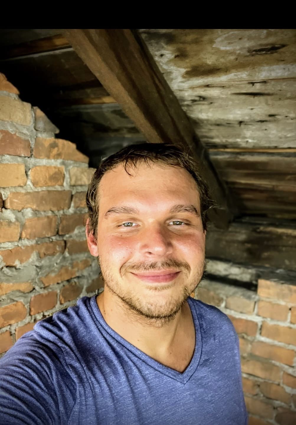 Frank Foust smiling in a room with exposed brick and unfinished wood beams